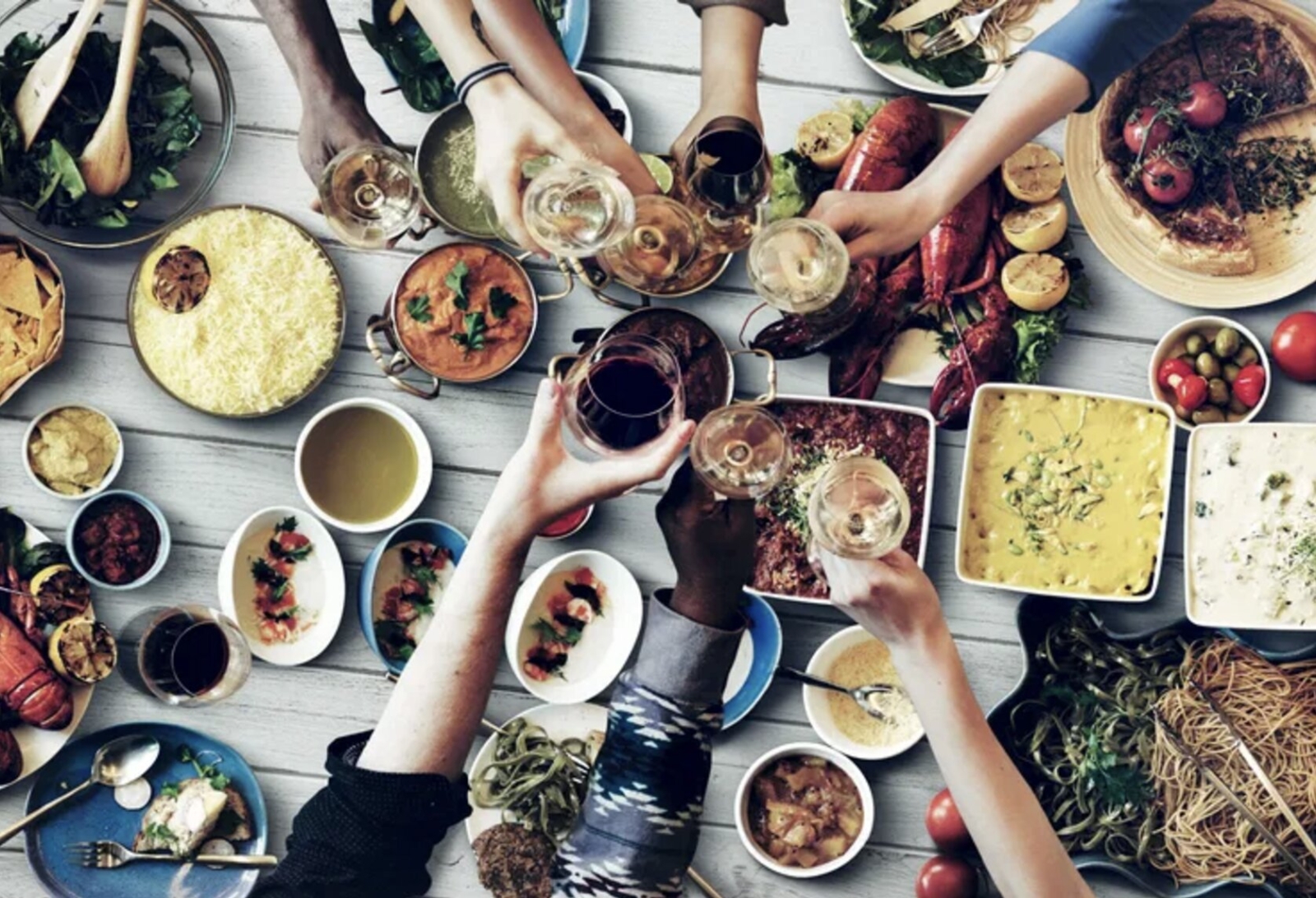 A group of friends raising their glasses in a toast over a diverse table spread of delicious food and drinks, celebrating togetherness.